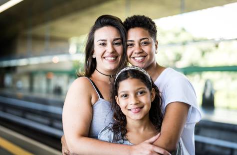 Female couple hugging their foster daughter at a train station