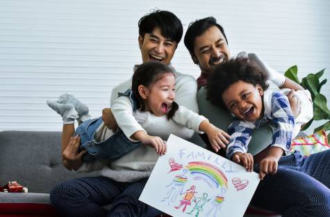 Male couple with their foster children who are holding a drawing of their family under a rainbow.