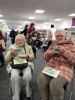 Two ladies sat in chairs drinking tea with books