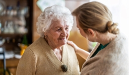 Person comforting elderly person with a hand on their shoulder