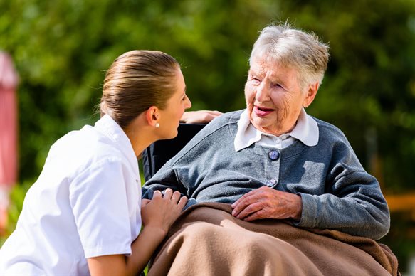 A nurse holding hands and talking to an older woman in a wheelchair.