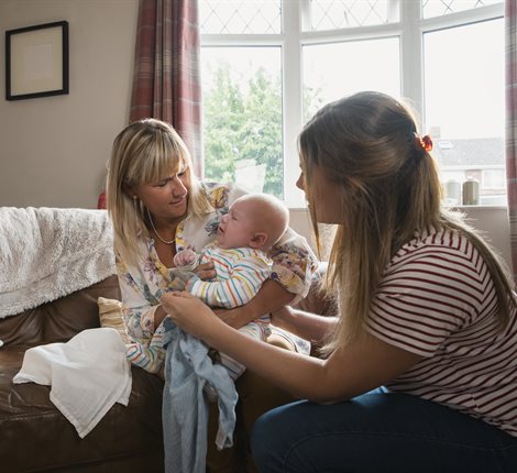 Two women holding baby on sofa