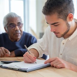 Older man helping a young man writing