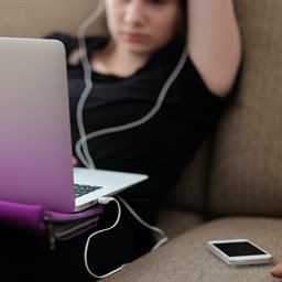 Young woman wearing ear pods looking at a macbook