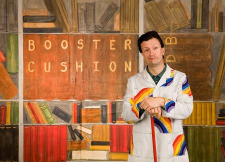 Man in a rainbow coat standing in front of a painted backdrop