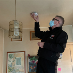 firefighter checking a ceiling fire alarm in a room.