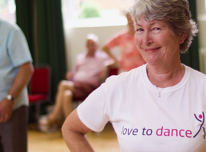 Older woman smiling and wearing a shirt that says 'love to dance'