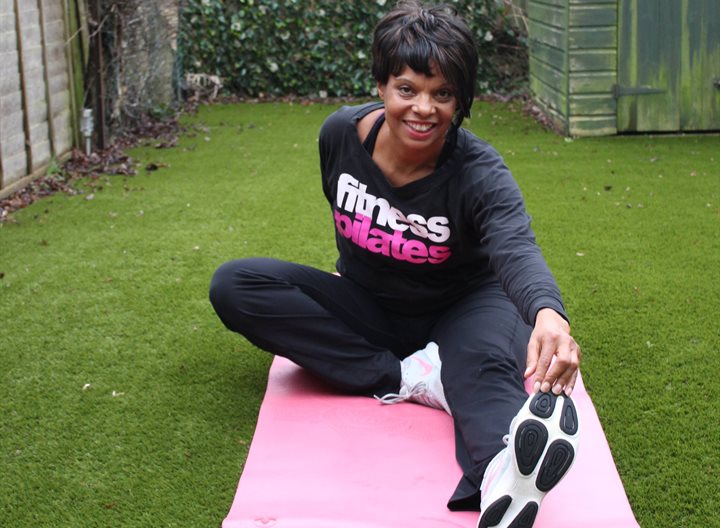 Lady sitting in garden on exercise mat stretching to touch her toes
