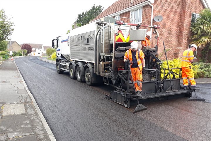 Men on a lorry spreading tarmac on a road