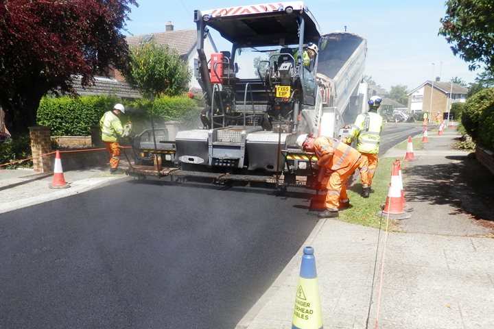 A large machine and men smoothing tarmac on a road