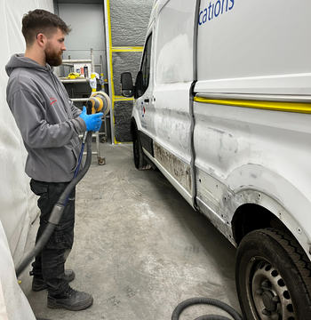 man spray painting a van in an auto body shop.