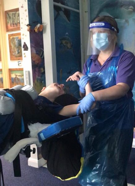 An image of a young person having a pysiotherapy session at home with the physiotherapist wearing full PPE